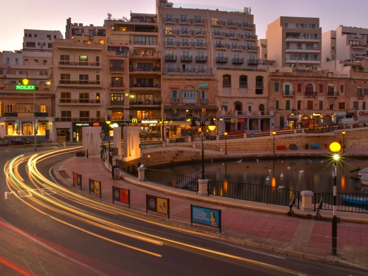 Long exposure photo of Saint Julian's Bay in Malta at sunset, showcasing vibrant city lights and architecture.