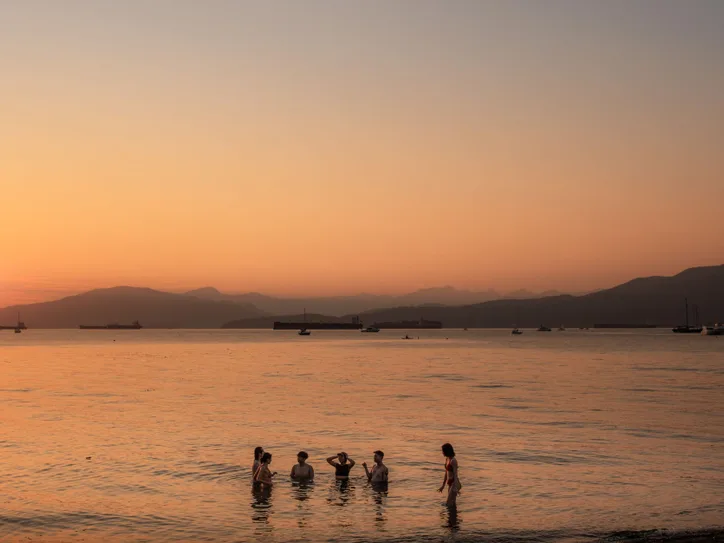 Silhouetted group of friends enjoying a sunset swim along the Vancouver shoreline.