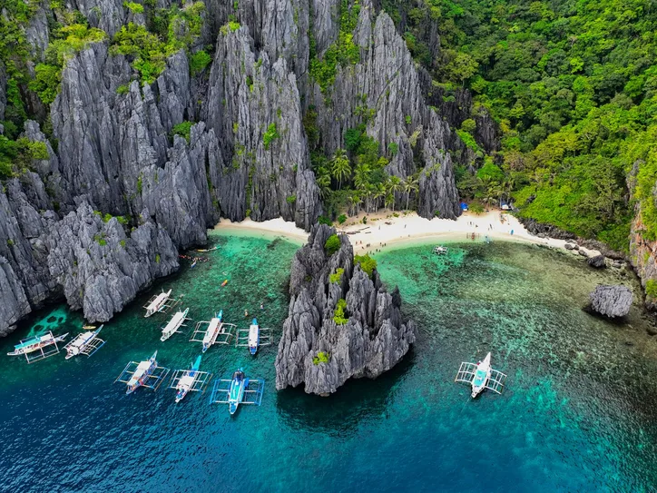Breathtaking aerial shot of El Nido's limestone cliffs with tour boats in turquoise waters.