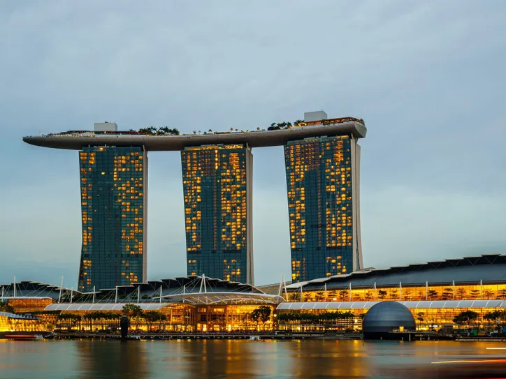 Marina Bay Sands illuminated at sunset in Singapore, reflecting on calm waters.