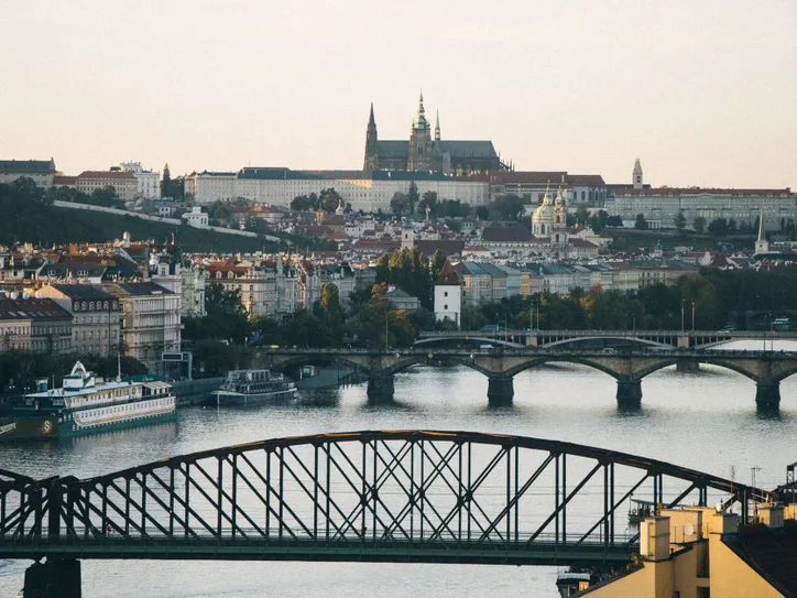 Scenic view of Prague's historic skyline, featuring the Vltava River and Prague Castle at sunset.
