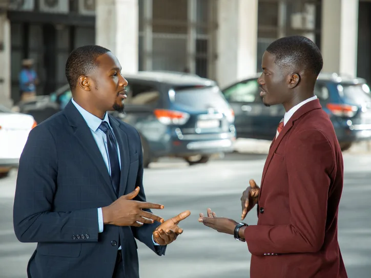 Two African businessmen in formal suits have a discussion on a city street in Dakar, Senegal.