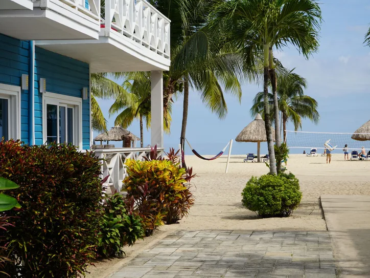 A vibrant beachfront villa in Placencia, Belize, surrounded by palm trees and a sandy beach with volleyball.
