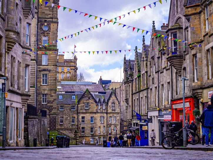 Lively Edinburgh street lined with historic architecture and festive bunting above. Perfect depiction of Scottish urban charm.