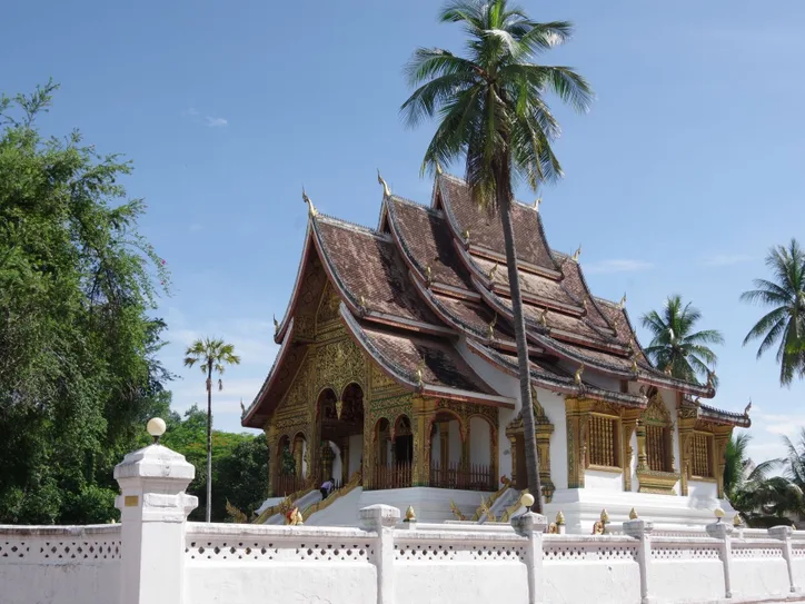 Explore the Royal Palace's intricate architecture surrounded by lush palms in Luang Prabang, Laos.