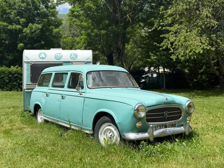 Charming vintage Peugeot and caravan parked in a lush, summer landscape in Saint-Lary-Soulan, France.