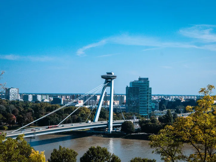 A scenic cityscape of Bratislava featuring the iconic UFO Bridge over the Danube River.