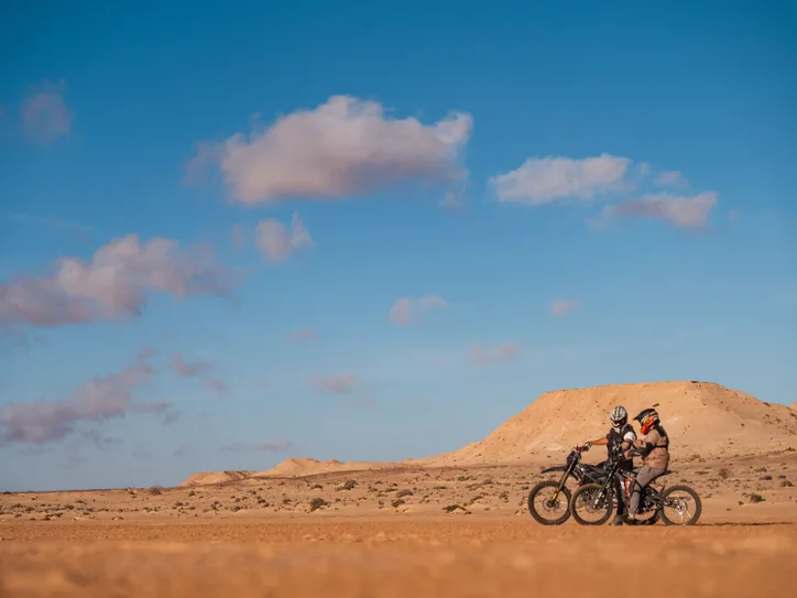 Two motorcyclists navigate the vast desert landscape of Dakhla under a clear blue sky.