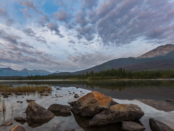 Tranquil lake scene with mountains and cloudy sky in Jasper National Park, Canada.