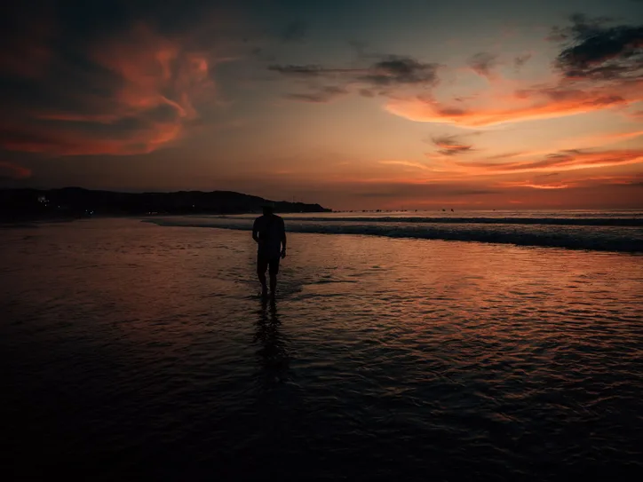 A man walking along the tranquil Máncora beach during a dramatic sunset.