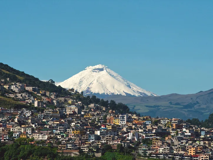 Explore Quito with the majestic backdrop of Cotopaxi Volcano under a clear blue sky.