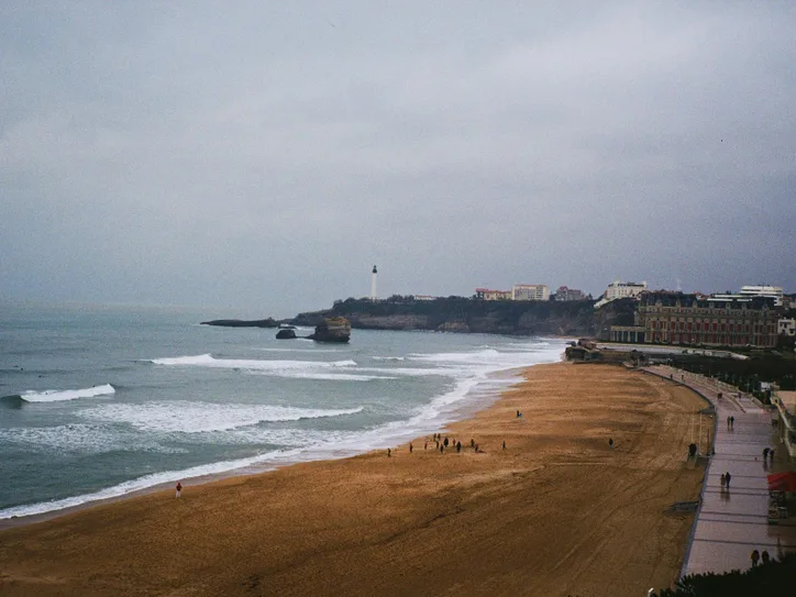 Beachfront and lighthouse at Biarritz with waves and cityscape in view.