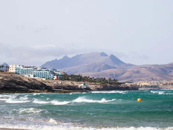 Scenic view of Fuerteventura coastline with waves and mountains in the background.