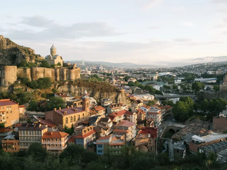 A scenic aerial view of Tbilisi featuring the historic Narikala Fortress at sunset.