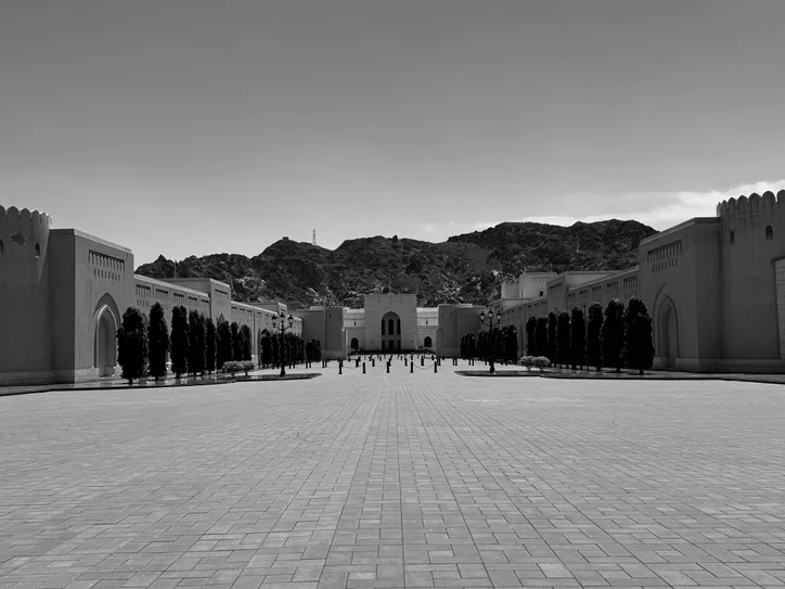 Black and white view of a striking architectural complex framed by mountains in Muscat, Oman.
