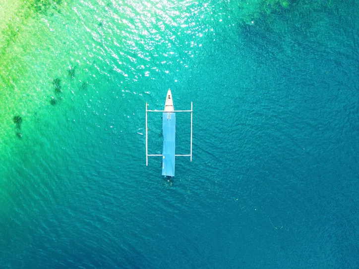 A drone capture of a boat floating on the vibrant turquoise waters of Lombok, Indonesia.