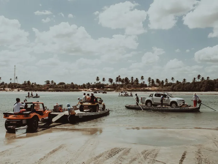Vehicles being ferried across a beach in Jericoacoara, Ceará, Brazil, with palm trees in the background.