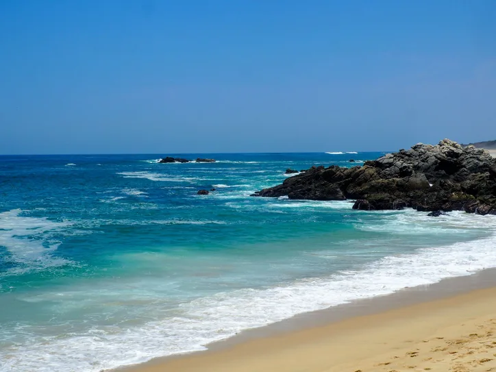 Tranquil view of Puerto Escondido's sandy beach with clear turquoise waters and rocky coastline.