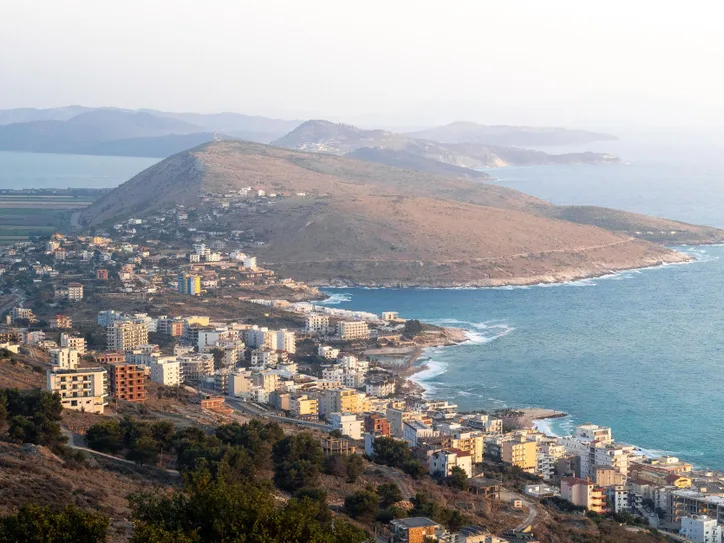 Explore the picturesque coastal view of Sarandë, featuring Lekursi Castle in the enchanting evening light.