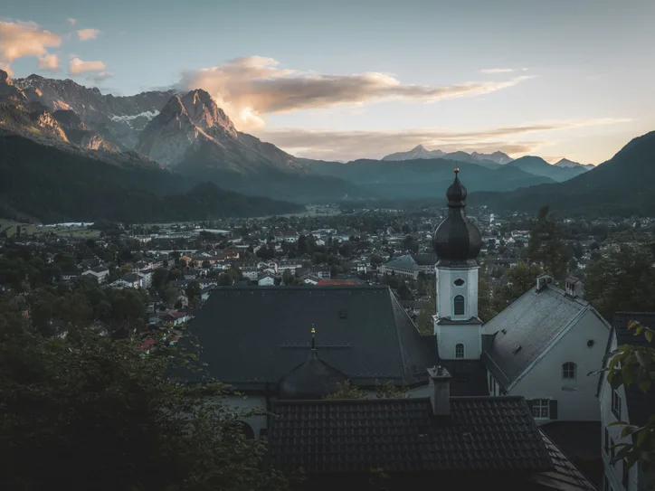 Breathtaking view of Garmisch-Partenkirchen with a church in the foreground and Alps at sunset.