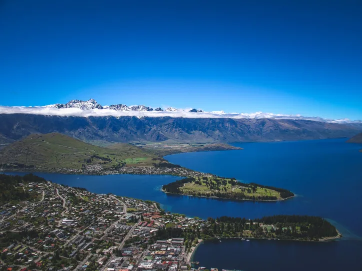Stunning aerial shot of Queenstown, New Zealand with clear blue lake and snow-capped mountains.