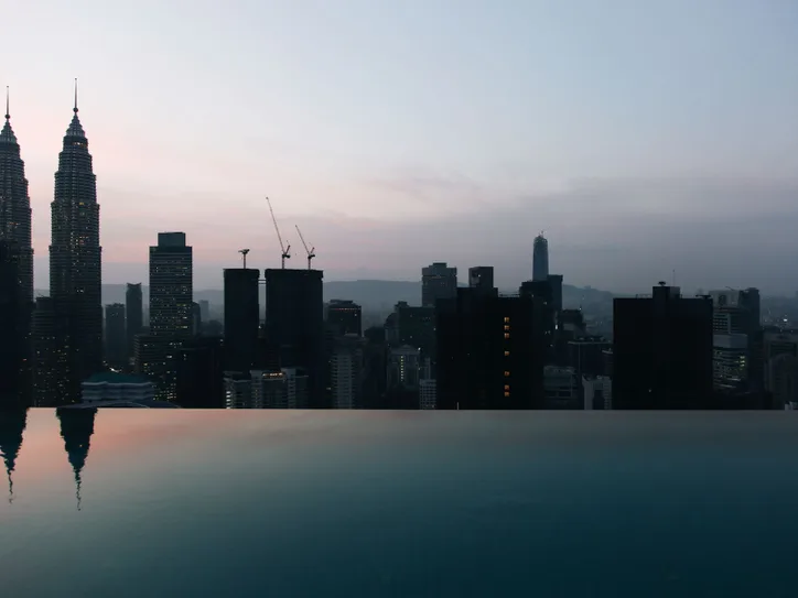 Twilight view of Kuala Lumpur skyline featuring the iconic Petronas Twin Towers reflecting in an infinity pool.