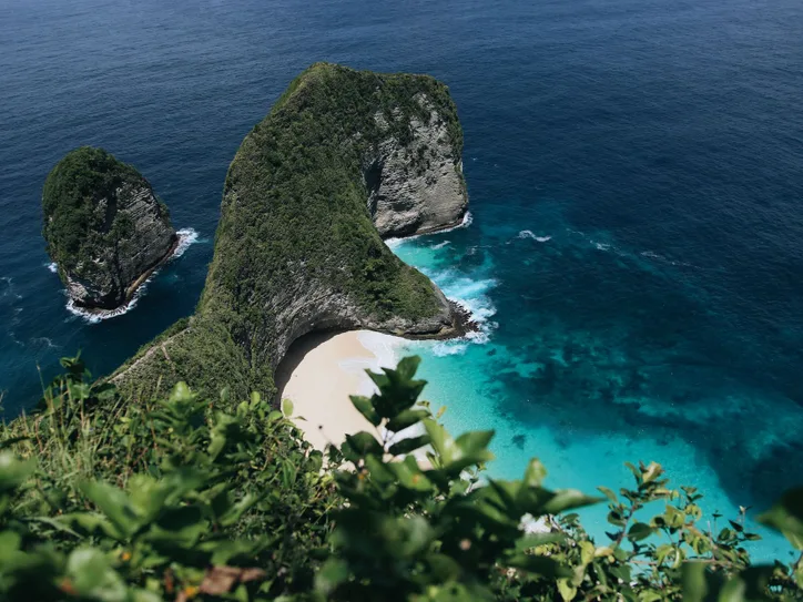 Stunning aerial view of Nusa Penida's picturesque beach in Bali surrounded by clear turquoise waters and lush green cliffs.