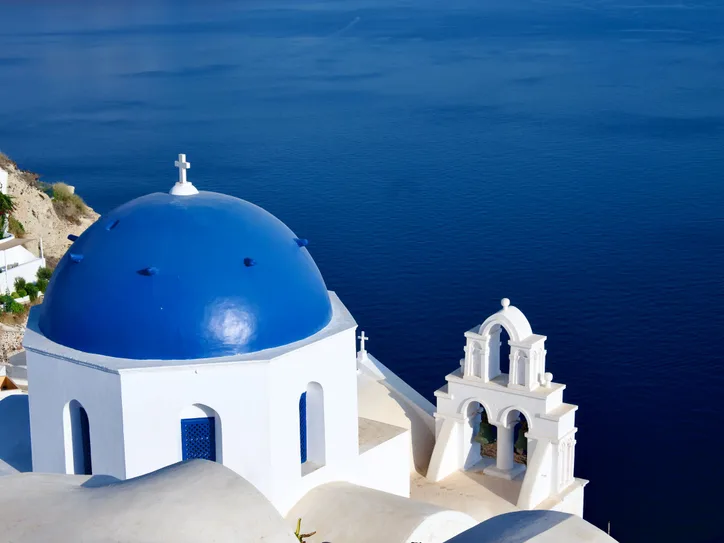 Breathtaking view of Santorini's blue-domed church overlooking the Aegean Sea, capturing Greek architecture.