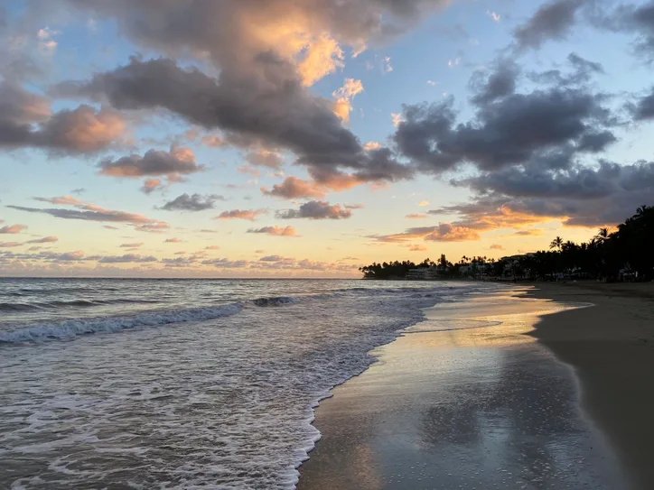 Serene sunset over Cabarete Beach with waves gently lapping the shore under a cloud-filled sky.