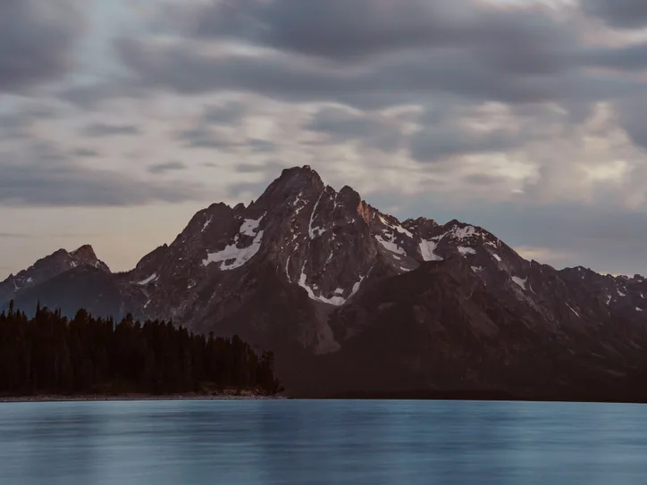 Breathtaking view of mountains and lake at sunrise with cloudy sky in Jackson, Wyoming.