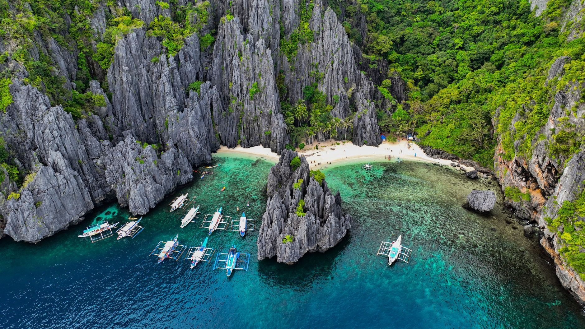 Breathtaking aerial shot of El Nido's limestone cliffs with tour boats in turquoise waters.