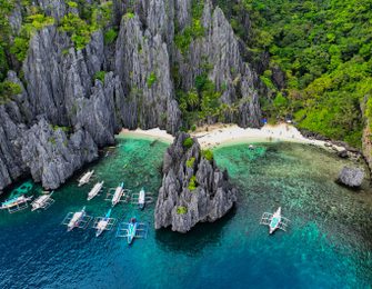 Breathtaking aerial shot of El Nido's limestone cliffs with tour boats in turquoise waters.