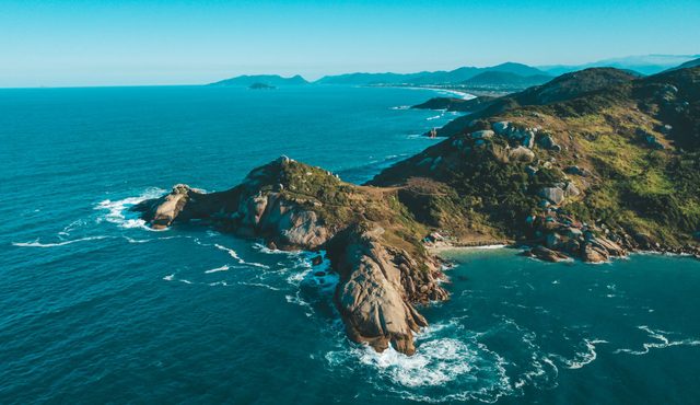 A breathtaking aerial view of the coastal landscape of Florianópolis, Brazil, with lush greenery and vibrant blue ocean.